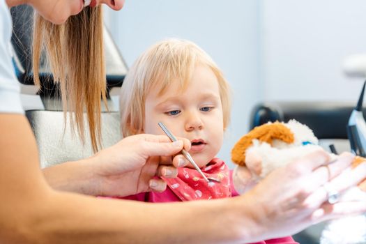 Dentist explaining treatment to a child using a plush toy, the little girl is watching