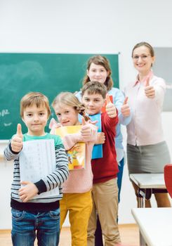 Pupils and teacher showing thumbs-up in school having fun in class