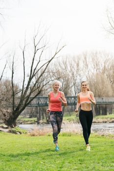 Senior woman with daughter running along the river away from the viewer