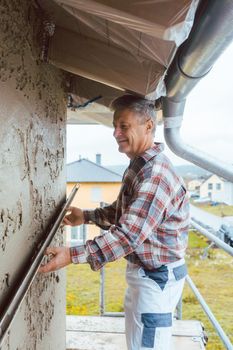 Plasterer smoothing plaster on a facade standing on scaffold