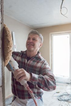 Plasterer man smoothing interior wall of new homes with machine