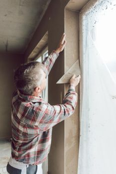 Diligent plasterer man or worker working on a window opening