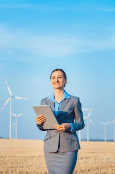 Investor in wind turbines with computer evaluating her investment on site looking pleased