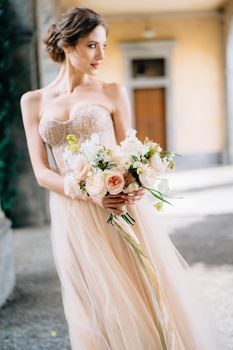 Bride in a beautiful dress with a bouquet of pink flowers stands in the vaulted hall with her head turned. Lake Como, Italy. Close up. High quality photo