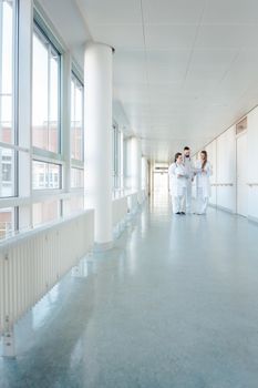 Three doctors on hospital corridor having short meeting discussing some cases