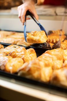 Woman selling fresh pastries in bakery shop, close-up on bread tongs