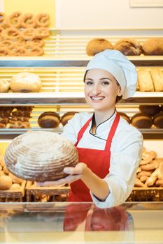 Saleswoman with apron presenting fresh bread in a bakery shop looking into camera