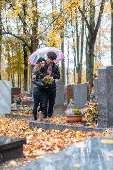 Couple mourning a deceased loved one on cemetery in fall standing between the graves