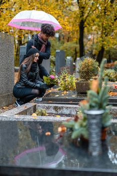 Couple in grief on a cemetery in fall while it is raining