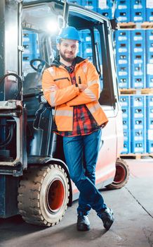 Worker in logistics distribution center leaning against his forklift