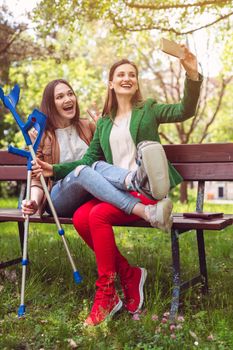 Best friends with one having a broken leg taking a selfie on the phone