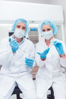 Scientists in biotech lab with pipette and sample dish looking into camera