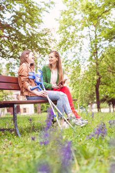 Two women, one healthy and one with a sprained foot, on a bench in the park