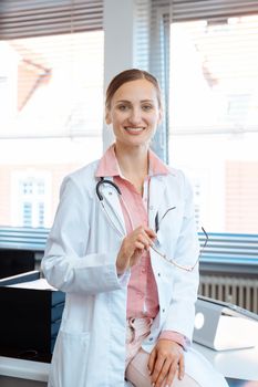 Smiling doctor woman standing at desk in her office