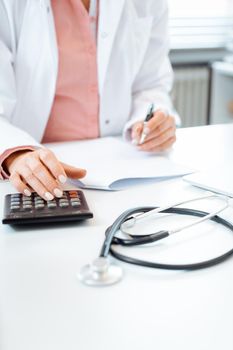 Closeup of doctor using calculator writing bills and doing bookkeeping