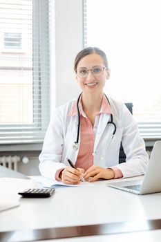 Beautiful doctor with computer in her surgery or office looking into the camera