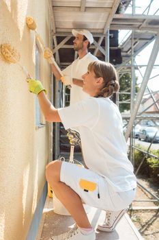 Woman painter painting a wall with yellow paint working hard