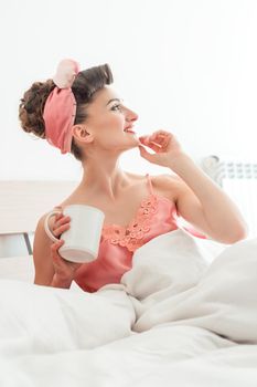 Woman waking up in her bed drinking a cup of coffee thinking about what the day will bring