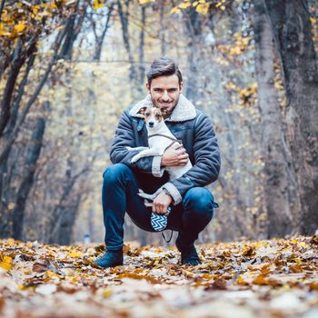 Young man walking his dog having a stroll in the autumn park snuggling with the pet