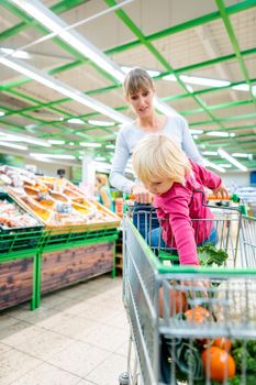 Mother having her toddler girl riding in shopping card of supermarket