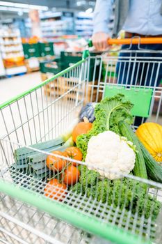 Man shopping in supermarket pushing his trolley with vegetables and groceries