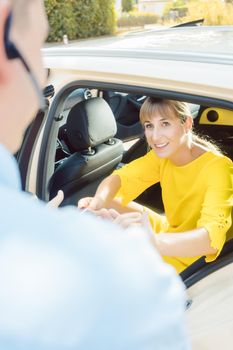 Taxi driver helping woman passenger out of the car carrying her bags