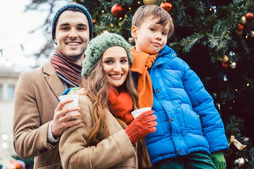 Family visiting Christmas Market standing in front of tree