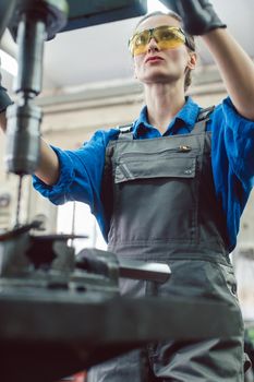 Woman worker in metal workshop using pedestal drill to work on piece