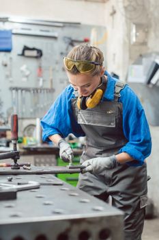 Woman mechanic working in metal workshop using clamps, screws, and spanner