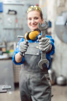 Woman mechanic showing tools to the camera holding wrench in her hand