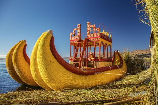 Reed boat on Island of Uros. Those are floating islands on lake Titicaca located between Peru and Bolivia. Colorful image with yellow boat and clear blue sky.