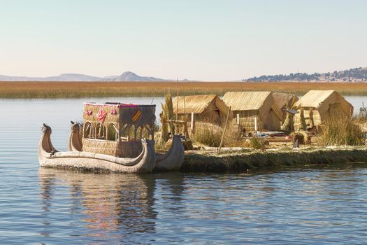 Reed boat on Island of Uros. Those are floating islands on lake Titicaca located between Peru and Bolivia. Colorful image with yellow boat and clear blue sky.