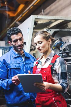 Woman and man manufacturing worker in discussion writing on tablet computer