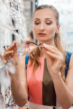 Woman shopping eyeglasses in optometrist store choosing between the models