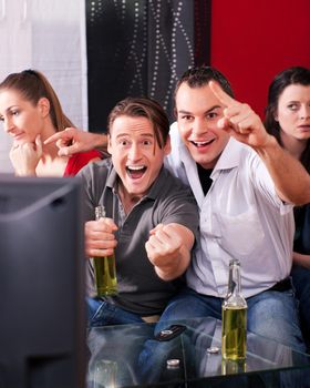 Two couples watching sports in the telly, the guys are really excited and cheer their team while the girls are quite bored