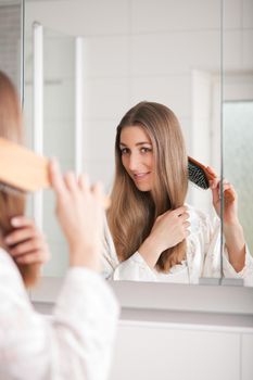 Young woman in pyjama brushing her long dark-blond hair after getting up in the morning