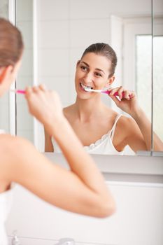 Young woman with light brown hair brushing her teeth after happily waking up in the morning