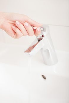 Woman (just hand to be seen) opening the water tap to wash her hands