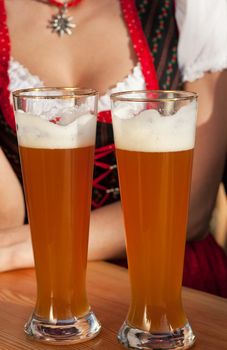 Couple in traditional Bavarian Tracht - Dirndl and Lederhosen - in front of a beer tent at the Oktoberfest or in a beer garden enjoying a glass of tasty wheat beer