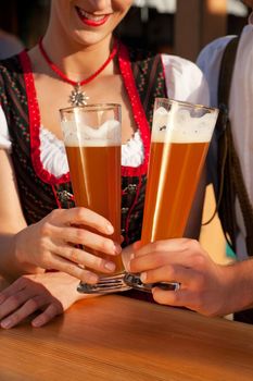 Couple in traditional Bavarian Tracht - Dirndl and Lederhosen - in front of a beer tent at the Oktoberfest or in a beer garden enjoying a glass of tasty wheat beer