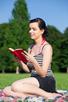 Woman reading book in the sunshine sitting on a meadow in summer