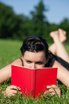 Woman reading book in the sunshine lying on a meadow in summer, FOCUS is on the book