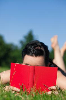 Woman reading book in the sunshine lying on a meadow in summer, FOCUS is on the book