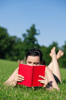 Woman reading book in the sunshine lying on a meadow in summer, FOCUS is on the book