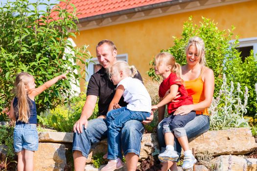 young family in front of home or house with three children sitting in the sun