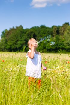 Little girl in field making soap bubbles and having fun with it