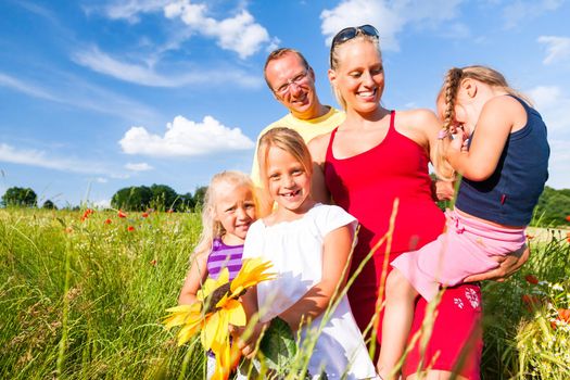 Happy family with tree kids standing in a field of wild flowers together