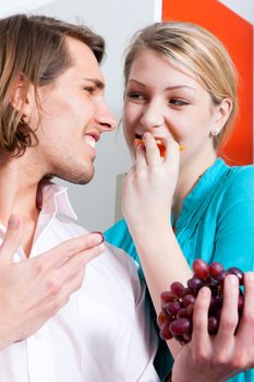 Couple eating bunch of grapes at home in their kitchen