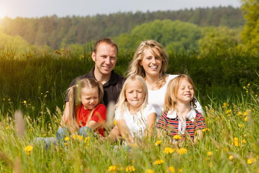 happy family with kids sitting in a meadow with dandelion in summer sun