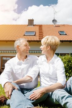 Senior couple of man and woman sitting in garden in front of home